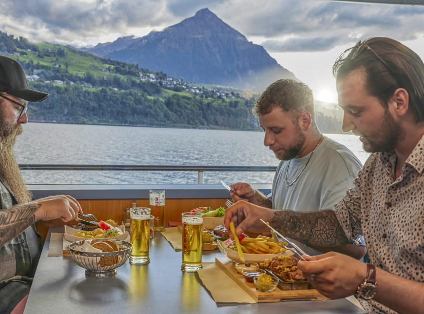 Gruppe von drei Freunden beim Essen auf Schiff mit Niesen im Hintergrund