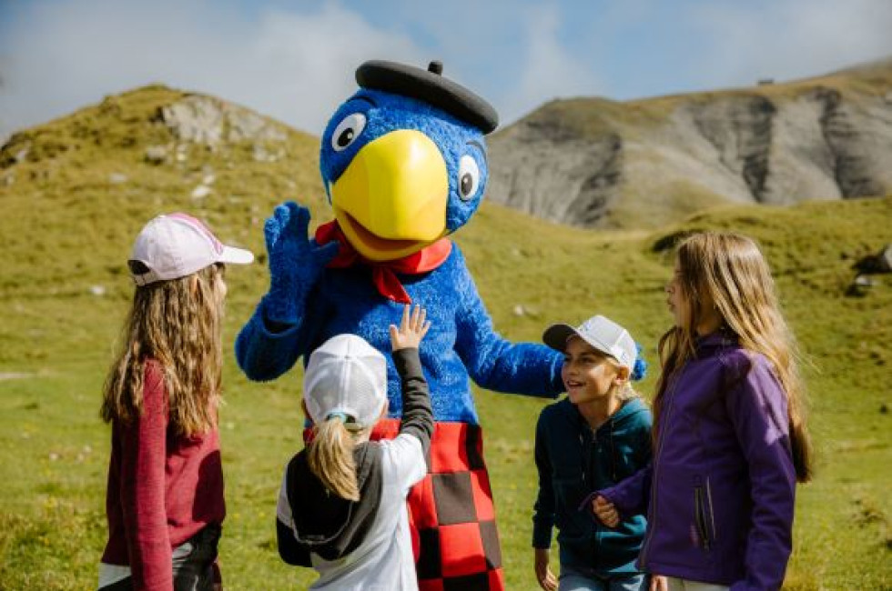 Globi umgeben von Kindern, im Hintergrund eine Berglandschaft