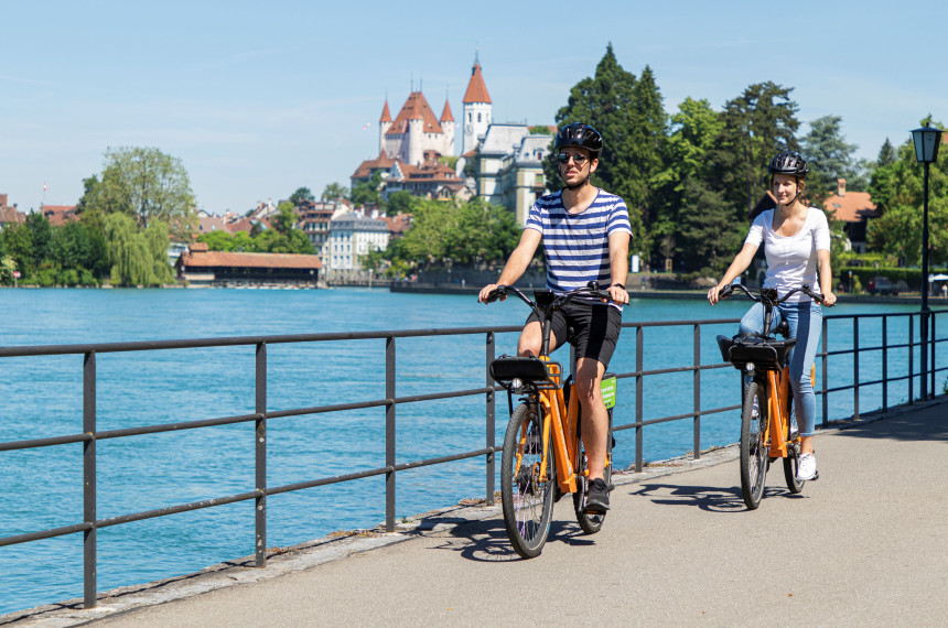 orangige Fahrräder mit Fluss und Schloss Thun im Hintergrund